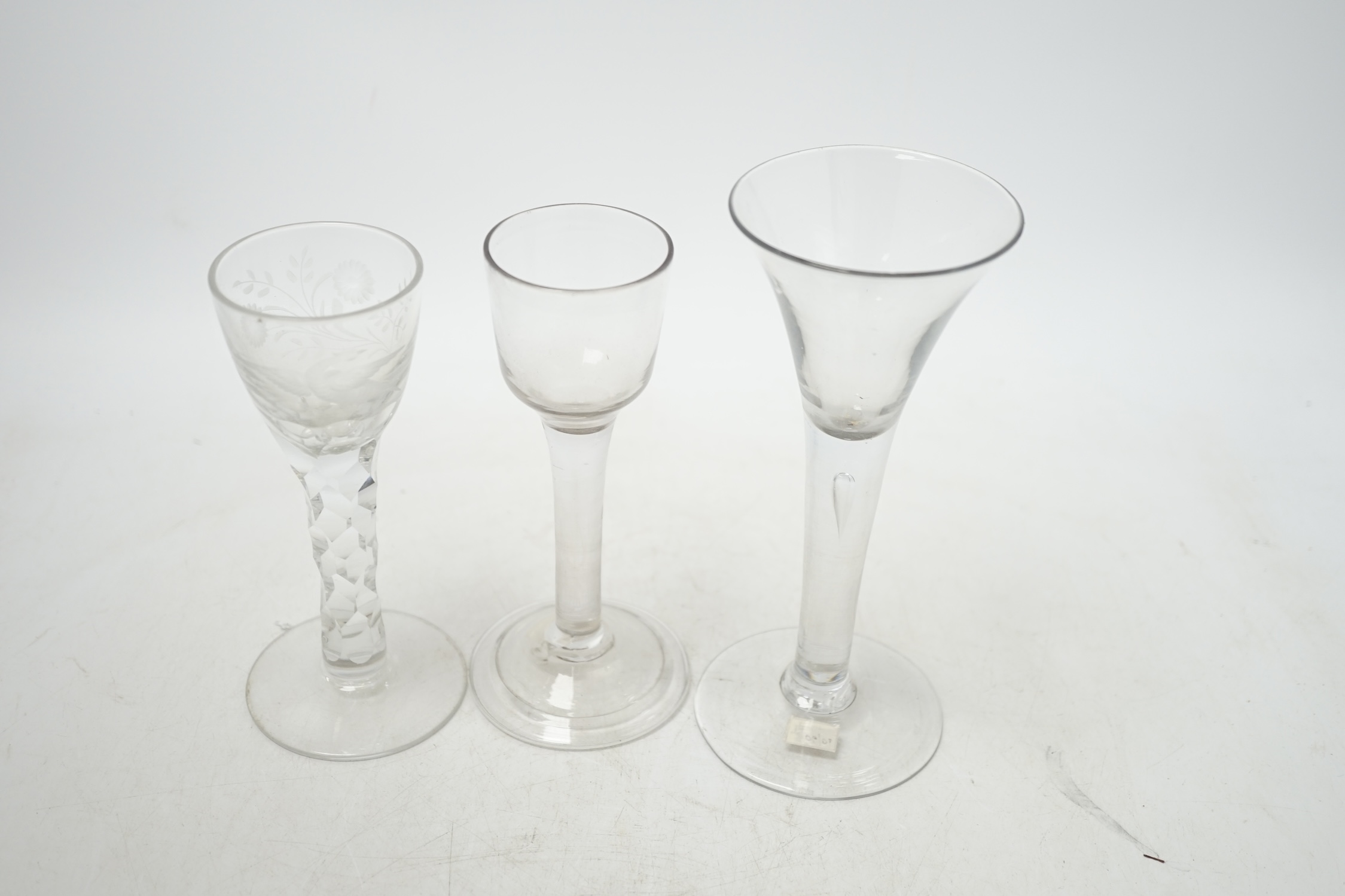 Three 18th century wine glasses; a drawn trumpet glass, another with a bell shaped bowl and folded foot and an engraved glass with a faceted stem, tallest 16.5cm. Condition - good